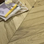 Close-up of chevron wood floor with books and a glass.