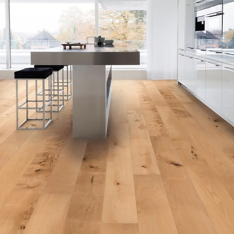 Light natural wood flooring in a modern white kitchen with a steel island.