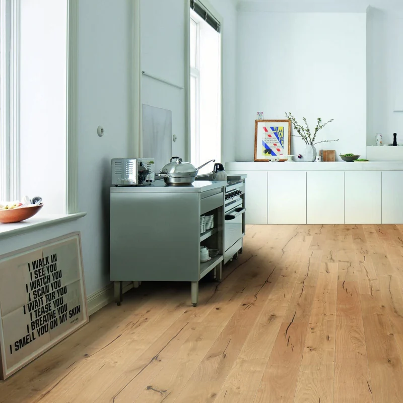 Light natural wood flooring in a modern white kitchen with a steel stove.